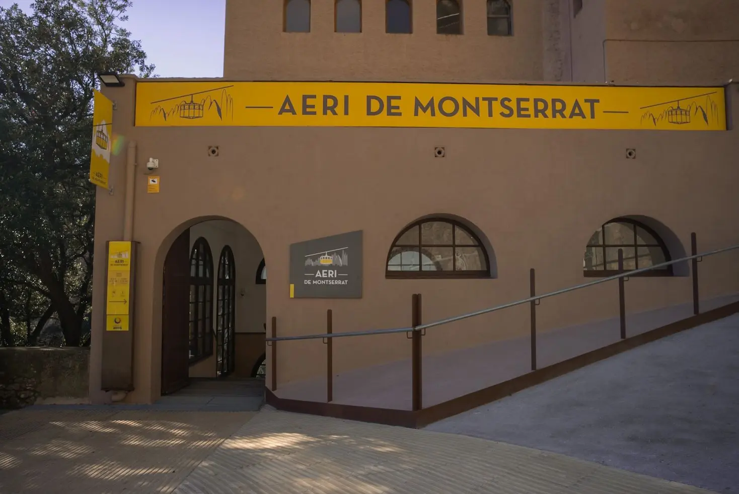 Entrance to the Aeri de Montserrat cable car station with yellow signage against a tan building facade.