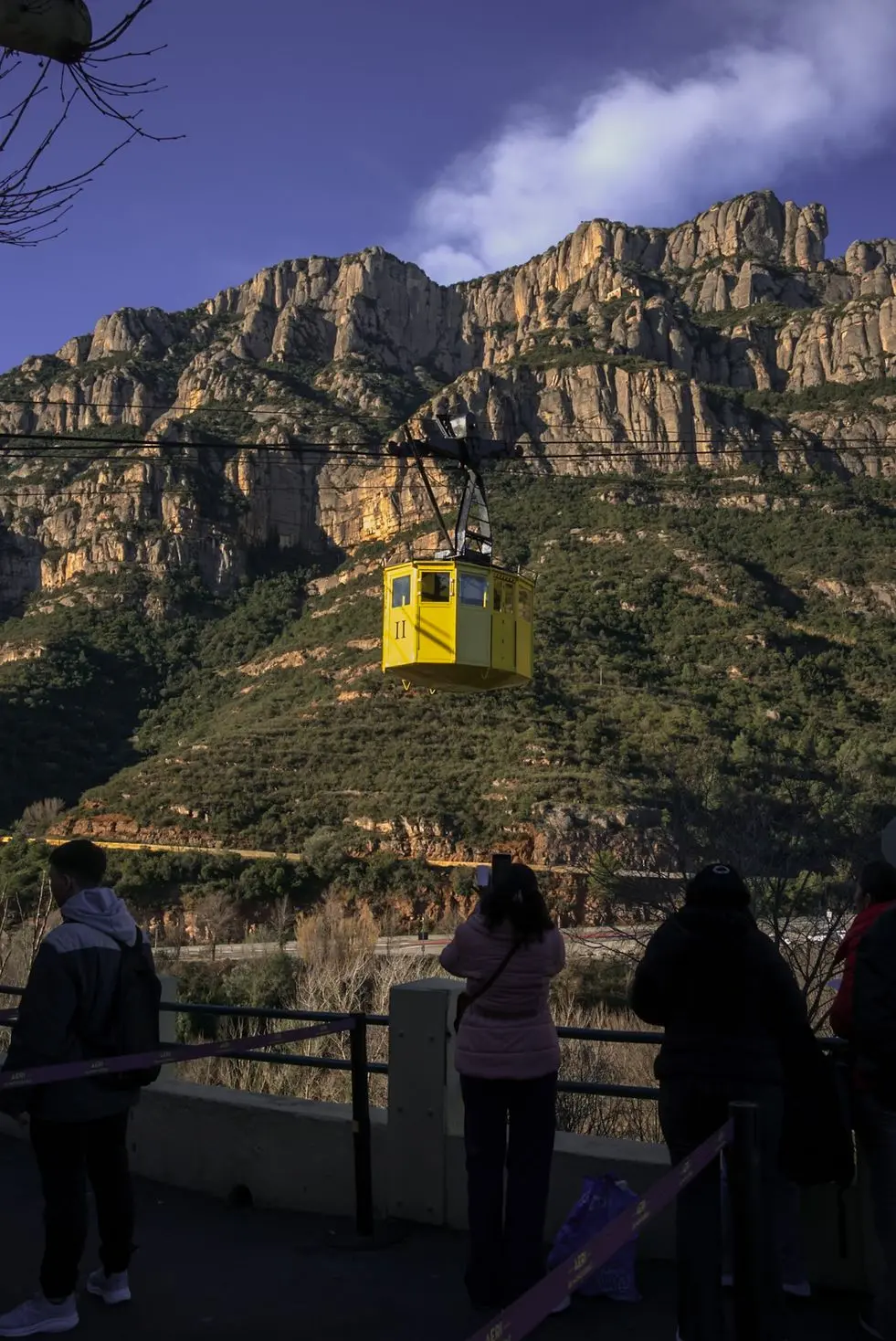 People watching the yellow Montserrat cable car ascend toward the jagged rock face in Catalonia, Spain.